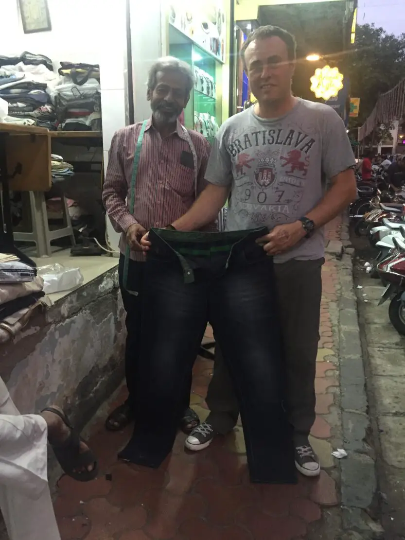 Andy holding a pair of jeans up with street tailor in Coloba in Mumbai, India