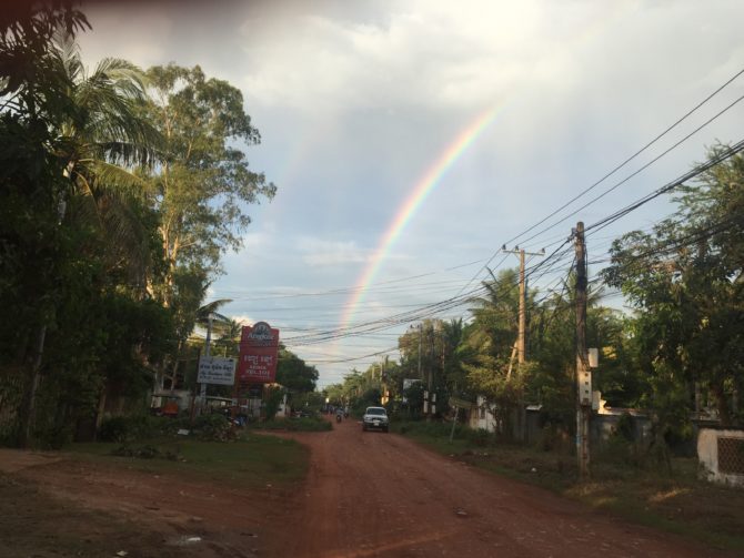 Red potholed dirt track with double rainbow overhead, in Siem Reap, Cambodia