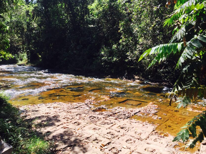 Kulen Mountain Cambodia 1000 Lingas carvings in the riverbed with green trees on the river banks.