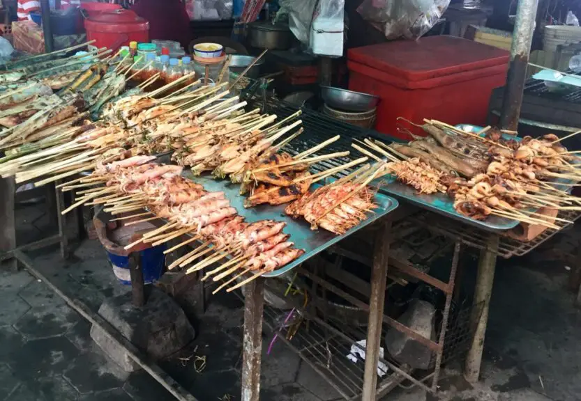 Kep Crab Market in Kep, Cambodia. Mountains of skewers of squid, prawns and other seafood on tables with a red esky coolbox in the background.