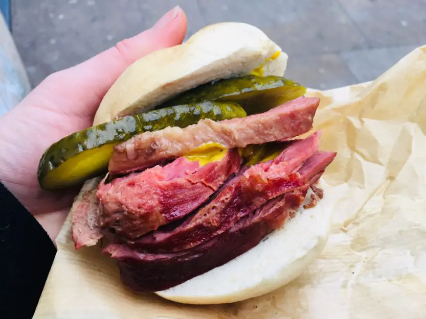 White bagel  with pink salt beef and green gherkin in a white from Beigal Bake in London, England