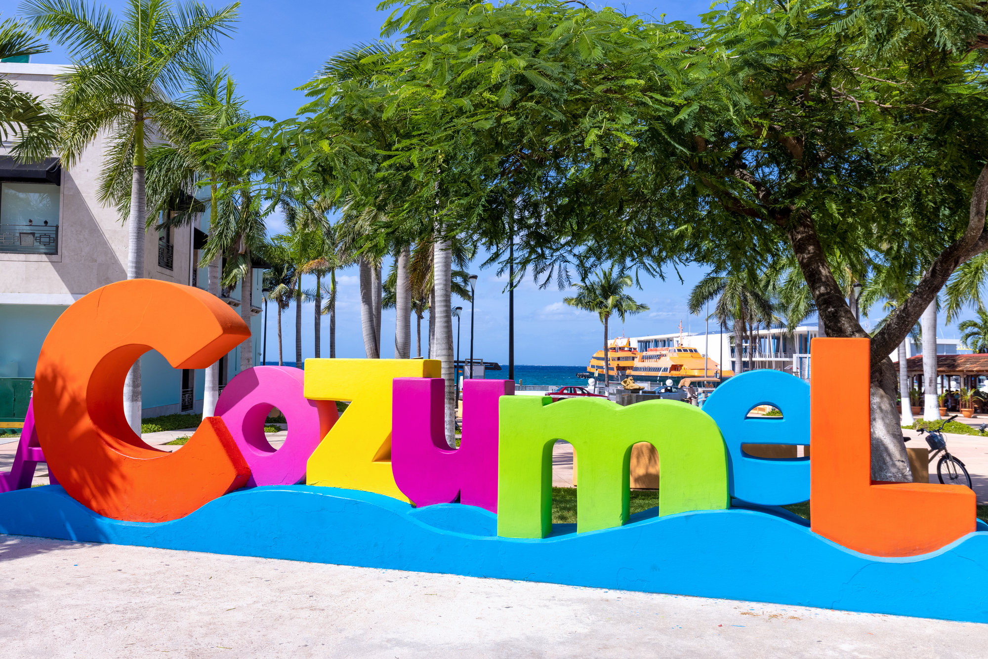 Colourful Cozumel sign with palm trees and the ferry port in the background