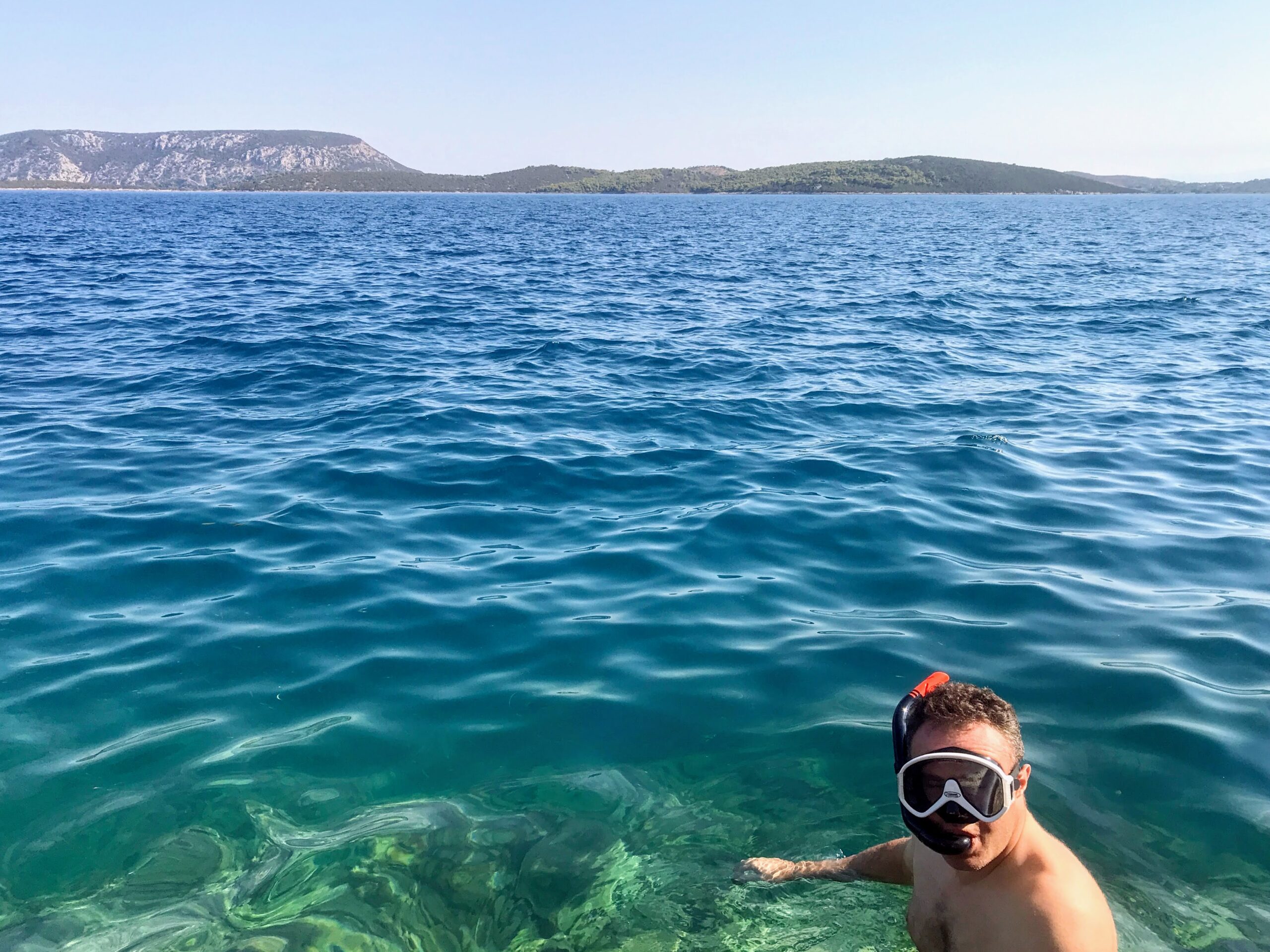 Andy snorkelling in the crystal clear sea on Mandrakia side of Ermioni in Greece. He's wearing a black and white snorkel mask and snorkel.