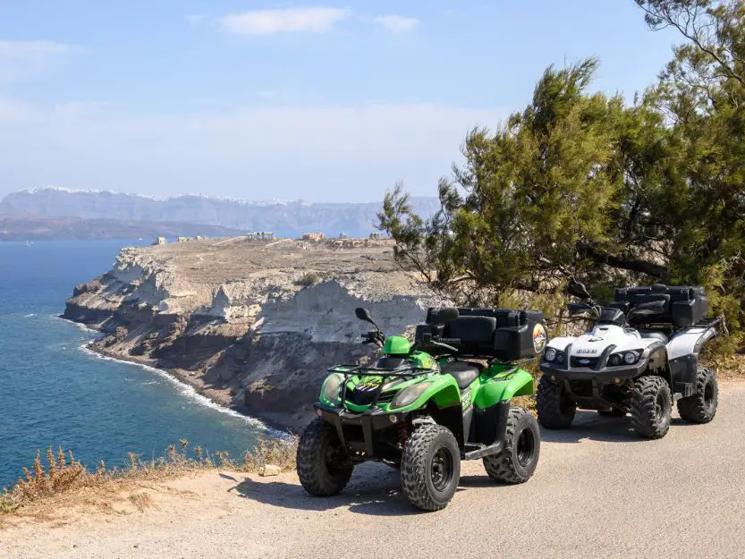 Green and white atvs on a road overlooking the sea on Santorini