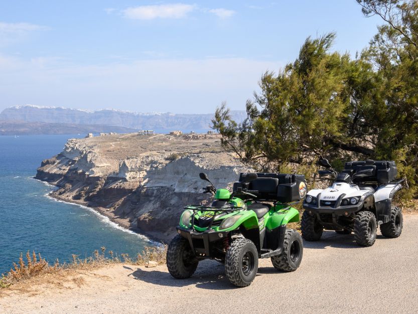 Green and white atvs on a road overlooking the sea on Santorini