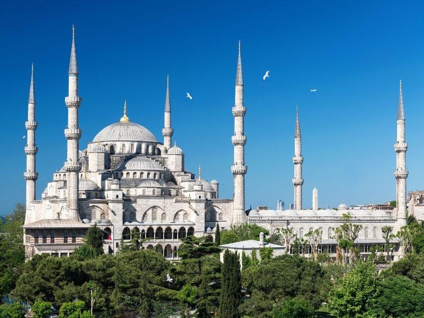 Blue Mosque Istanbul with blue sky background and green trees in the foreground.