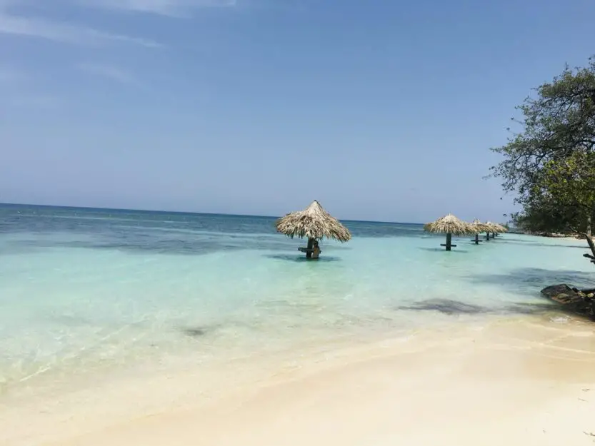 Chepes Beach on Utila, white sand with clear blue sea and palm parasols in the sea.