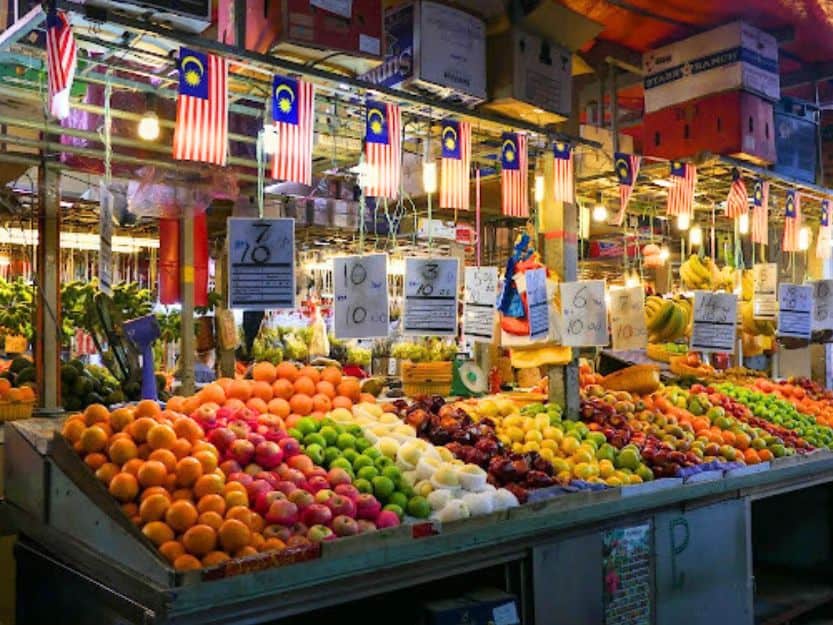 Chow Kit Market in Kuala Lumpur Chow Kit Market in Kuala Lumpur with a colourful fruit stall with prices and flags hanging above.