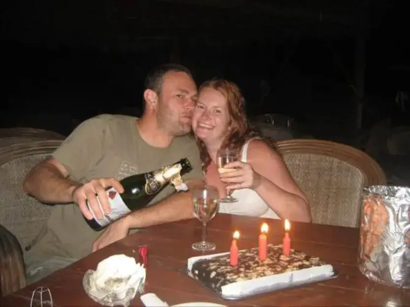 Our Story Can Travel Will Travel. Tanya and Andy with a bottle of bubbly and big chocolate cake with candles.