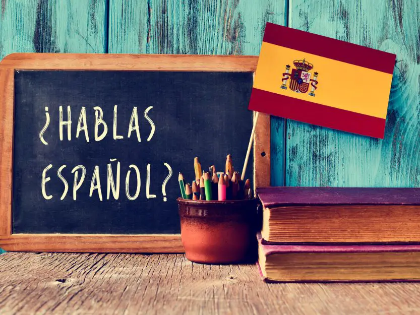 Blackboard with Hablas Espanol - Do you speak Spanish? on it - with a Spanish flag to the right. Red, yellow and red horizontal stripe with Spain coat of arms