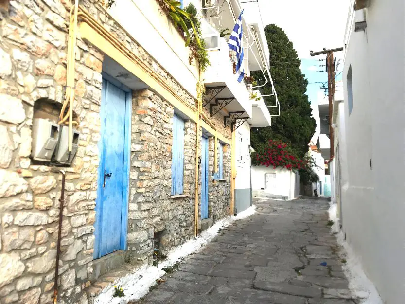 Cobbled back street of Ermioni town. To the left a stone house with blue doors and shutters.