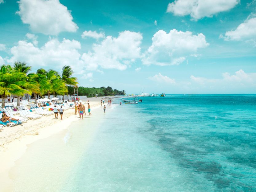 Ferry to Cozumel in Mexico - image of long white sand beach with blue sea to the right and palm trees to the left