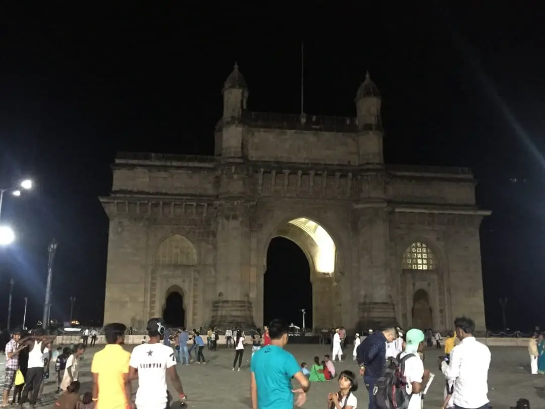 Gateway of India in Coloba Mumbai lit up at night with many people in the foreground.
