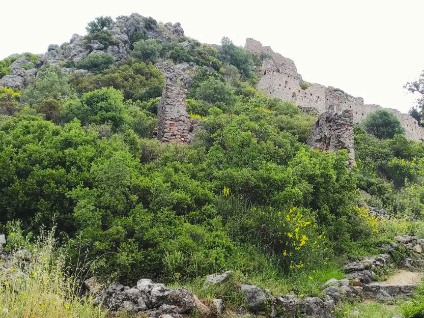Geraki Castle on top of a hill in Laconia. The grey stone ruins of the castle and fortifications are covered in greenery and wild flowers.