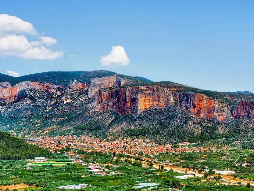 Leonido in Peloponnese, Greece. Red limestone rocks towering over the town with green trees in the foreground.