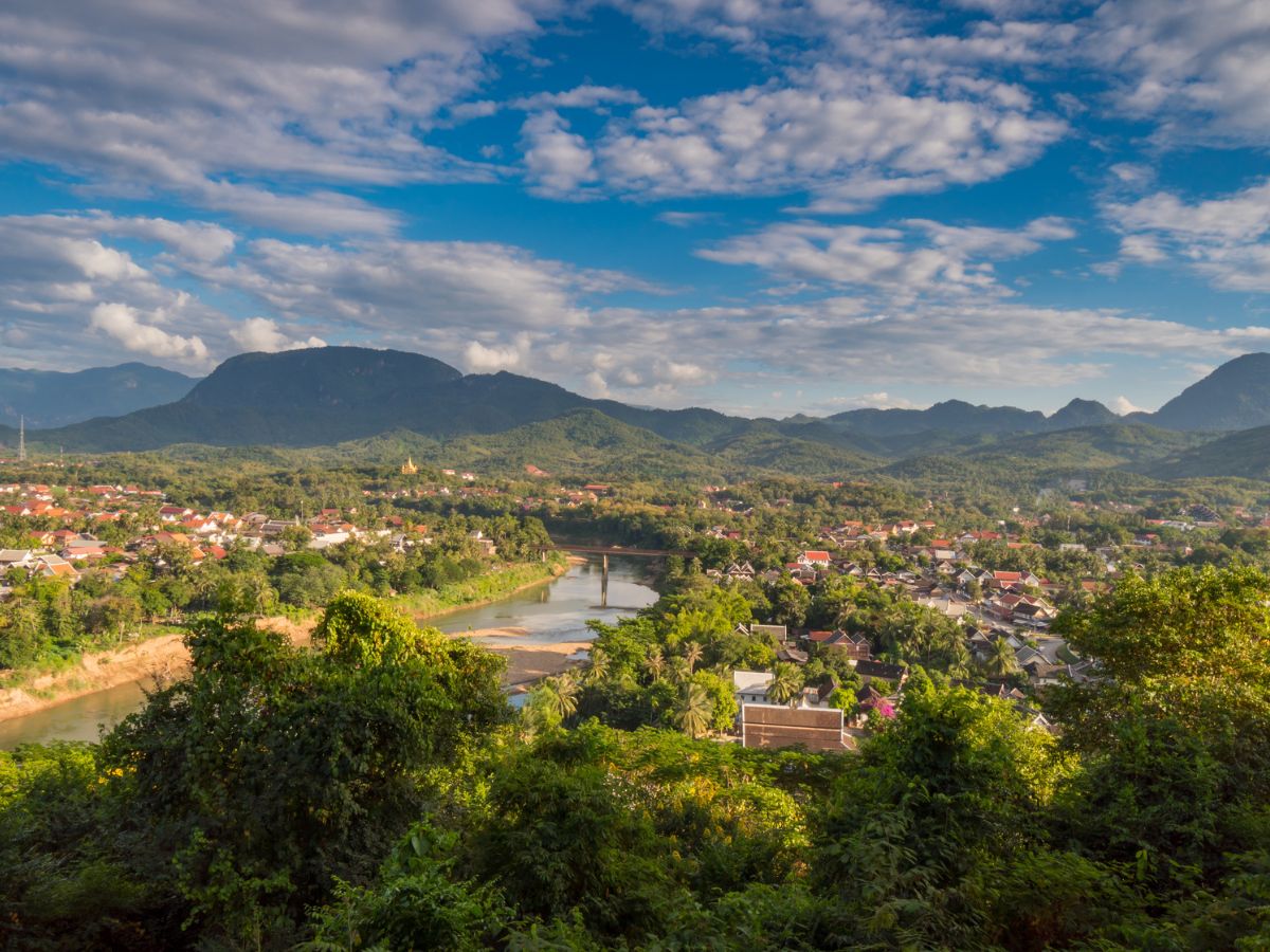 3-Day Luang Prabang Itinerary, Laos - aerial view of the town with blue sky and white clouds above and green trees in foreground