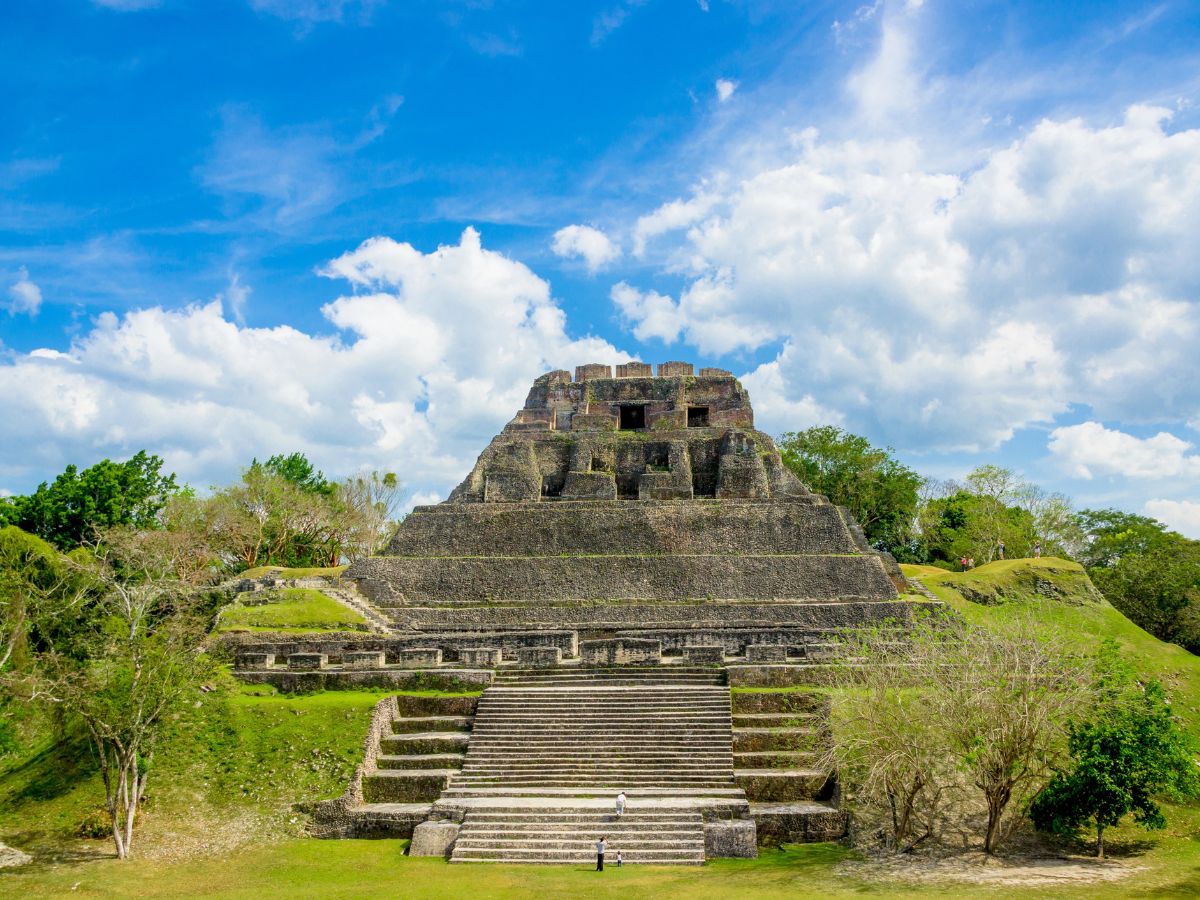 Mayan Ruins of Xunantunich in Belize. Stone pyramid surrounded by green grass, with blue sky and white clouds in the background.