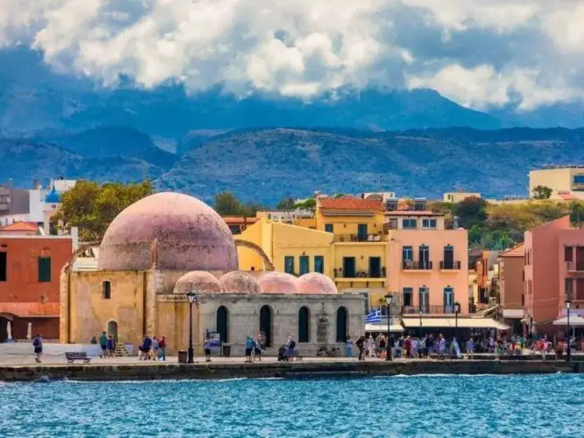 Colourful Mosque of the Janissaries on the clear blue water harbour in Chania, Crete.