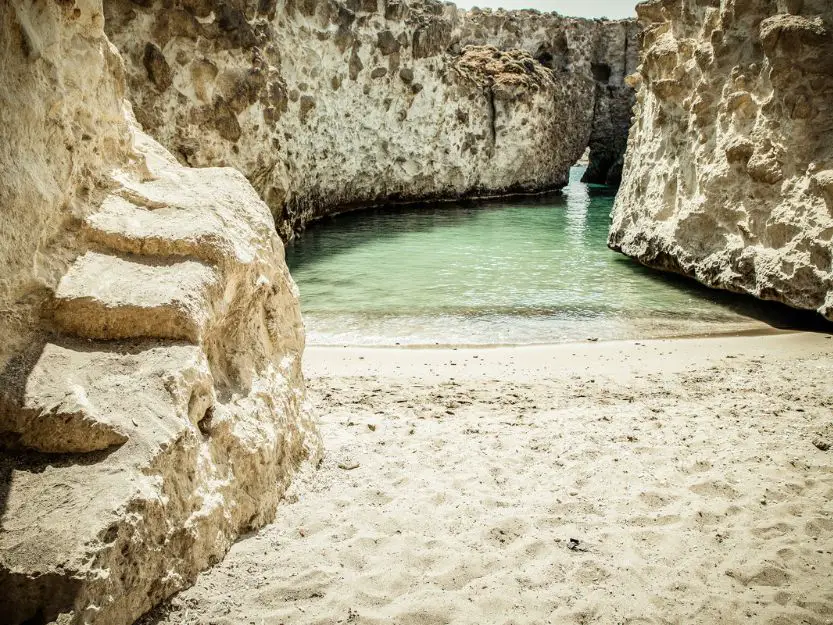 Papafragas Cave Beach on Milos in Greece. Sheltered pool with small sandy beach, that opens up into the sea through a natural arch.