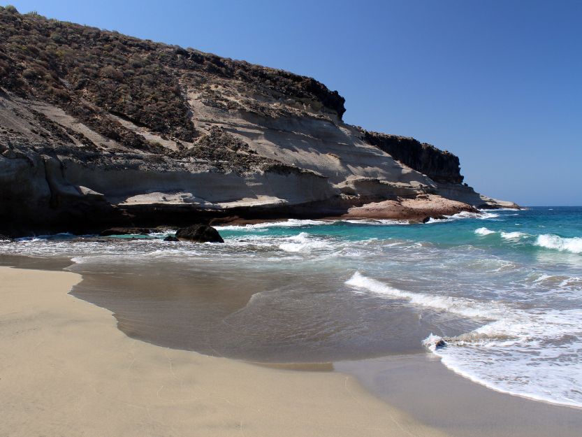 Playa Diego Hernandez, image of sandy bay on the left with cliffs on the left and blue sea on the right