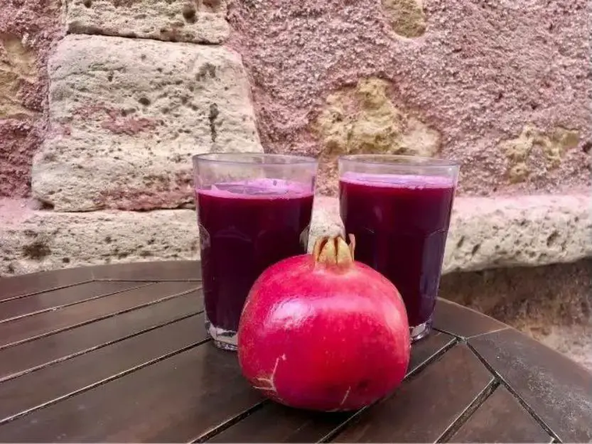 Fresh pomegranate juice in Chania on a table with a pomegranate fruit in front of the two glasses of juice.