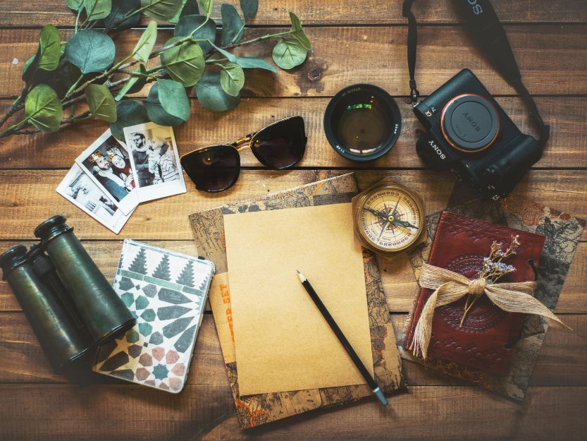 Reasons to Use SafetyWing Travel Insurance. Sunglasses, DSLR camera, binoculars, passport, notepad and photos on a wooden table.