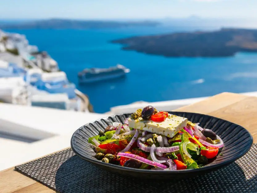 Greek salad on table in Santorini with the sea in the background.