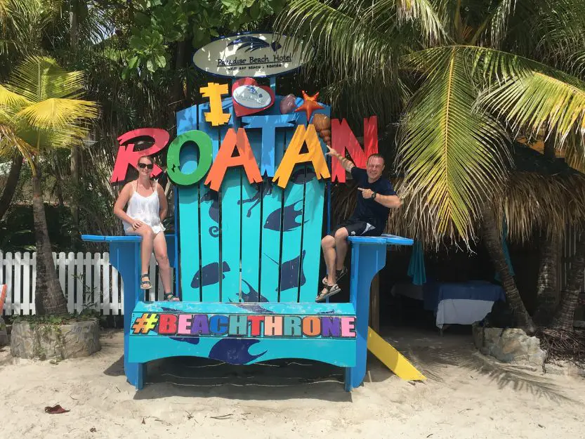 Tanya and Andy sitting on colourful wooden beach throne on Roatan Island in Honduras