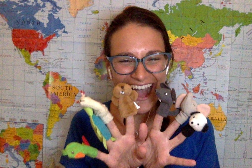 Teaching English Online to childre. Nicola Rae sitting in front of a wall map smiling with finger puppets.