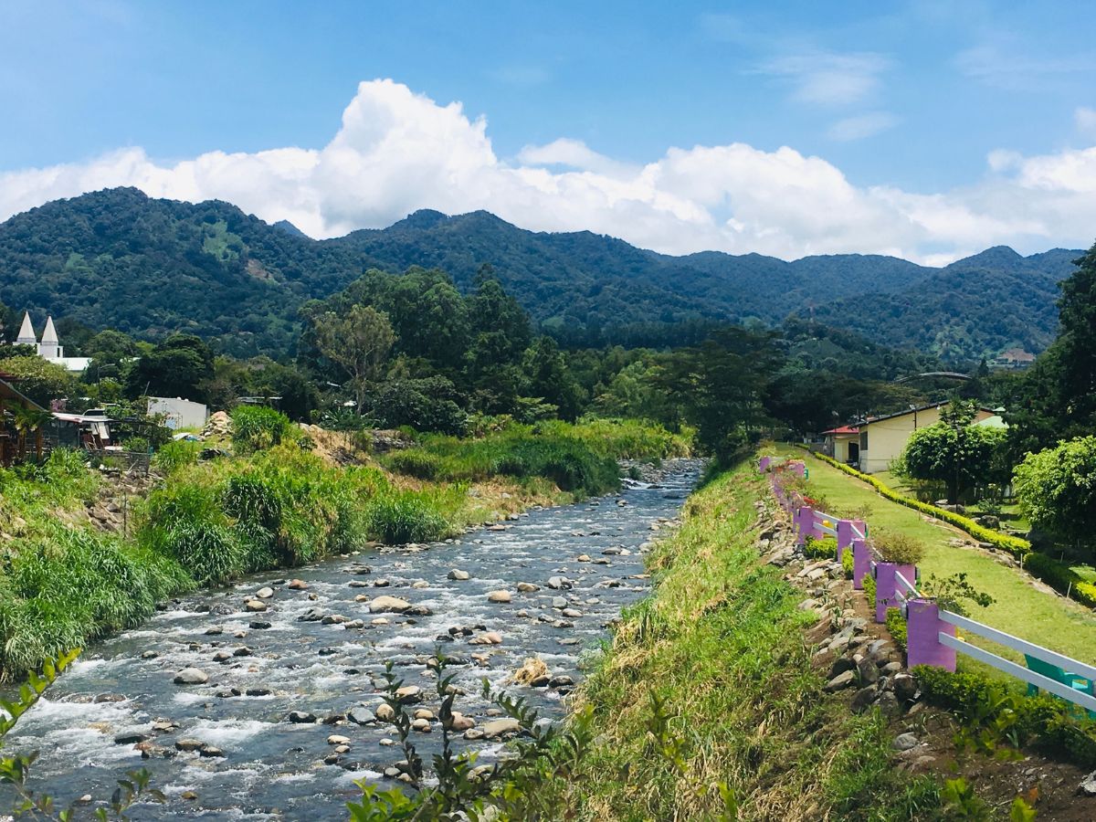 Things to Do in Boquete in Chiriqui, Panama. River with green banks and mountains in the background under white clouds and blue sky.