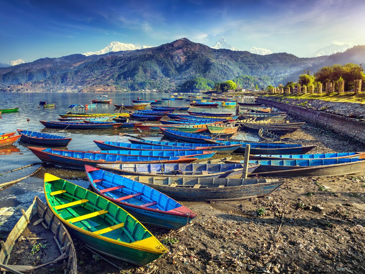 Things to Do in Pokhara Nepal. Colourful wooden boats at the edge of of Pokhara lake with mountains in the background.