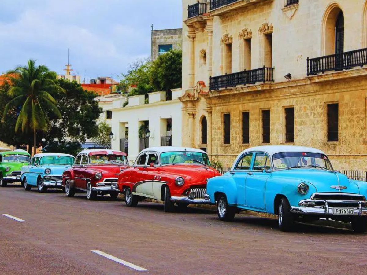 Independent travel to Cuba - image of old cars lining the street in cuba in front of a yellow building