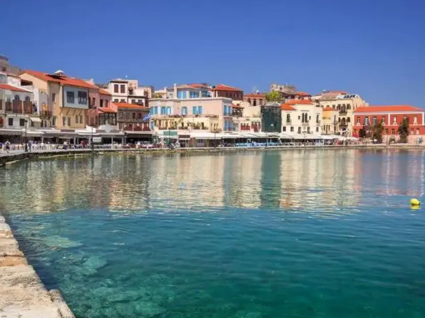 Venetian Harbour in Chania, Crete. Colourful buildings around the harbour with clear blue water in the foreground.