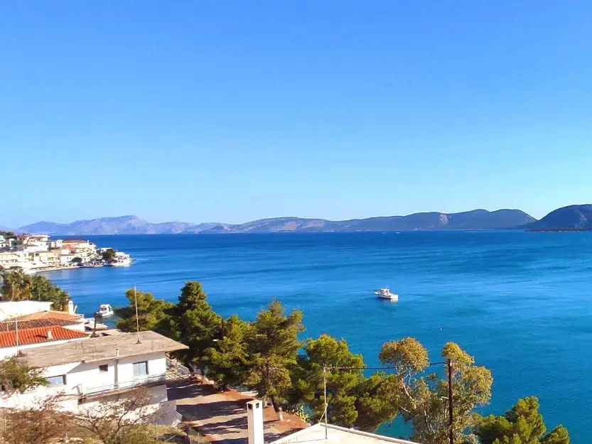 View of Madrakia side of Ermioni, Greece from Grand Bleu Apartments. Blue sea, green pines and the port side.