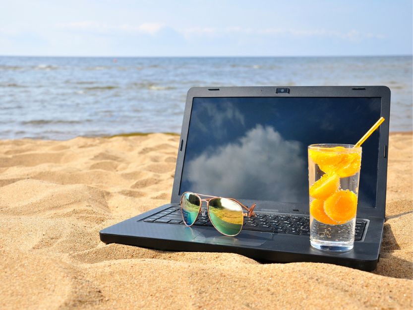 Laptop on a yellow sand beach with sunglasses and cocktail.